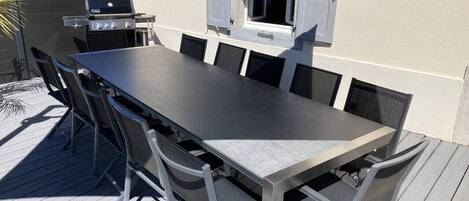 Un espace de restauration en plein air avec une longue table et des chaises, un barbecue et une fenêtre avec des volets.