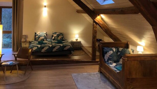 Une chambre mansardée chaleureuse, avec un plafond en pente, une lucarne, un lit, une chaise et une petite table.