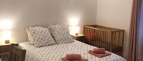 A bedroom with a bed, bedside tables, a wooden crib, and a chair.