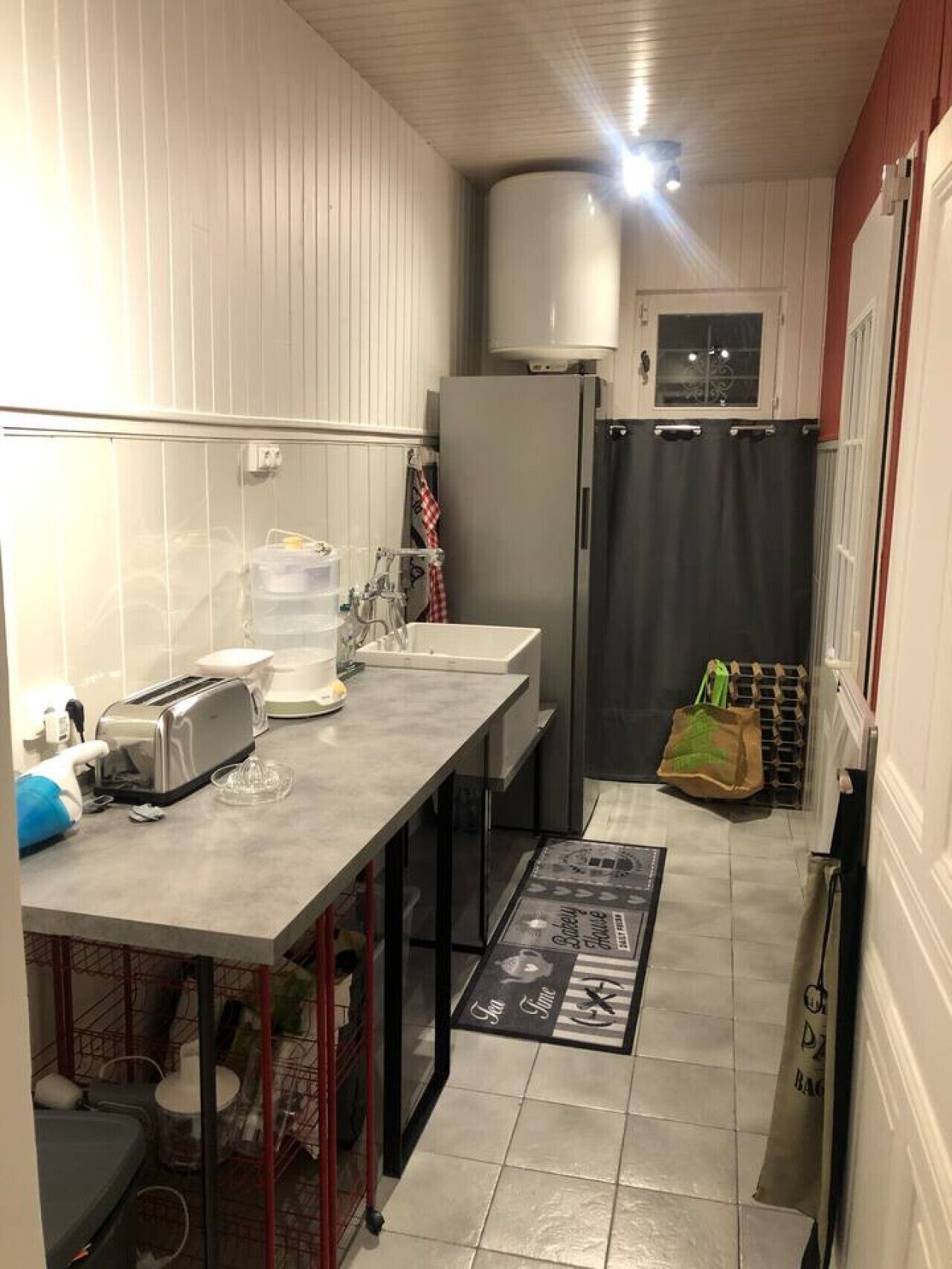 A compact kitchen with a refrigerator, a sink, and a toaster. There is a mat with a logo on the floor.