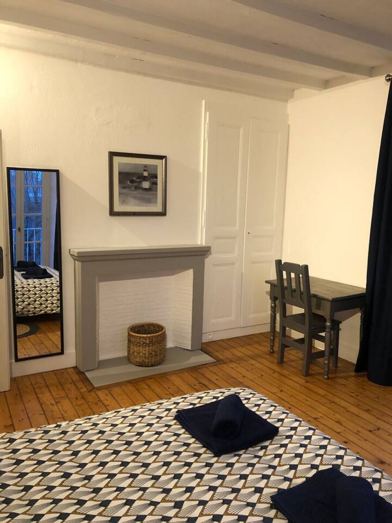 A room with a fireplace, a bed with a patterned bedspread, a desk, and a chair.