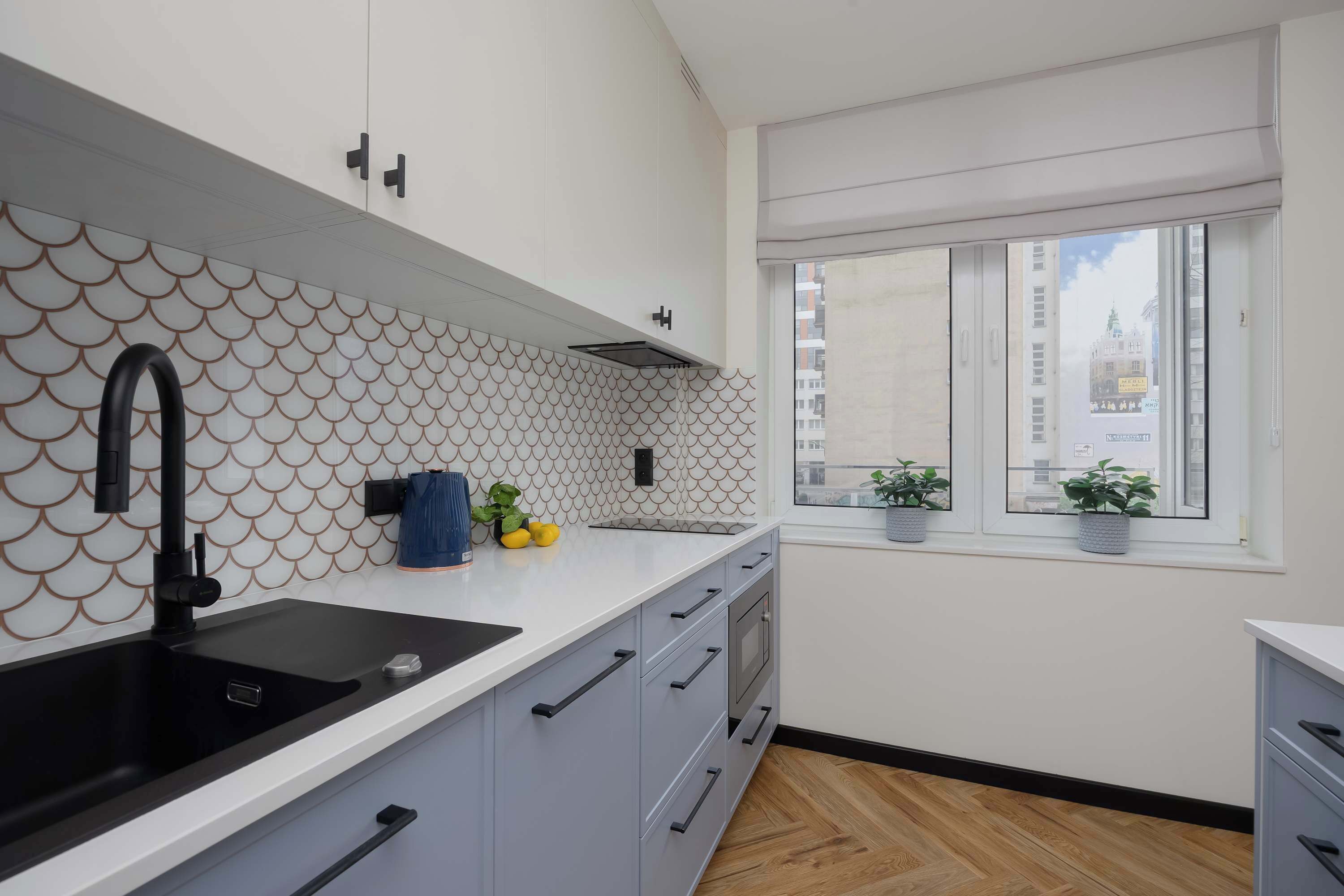 Eine moderne Küche mit einem schwarzen Spülbecken, grauen Schränken und einem Fenster mit Blumentöpfen.