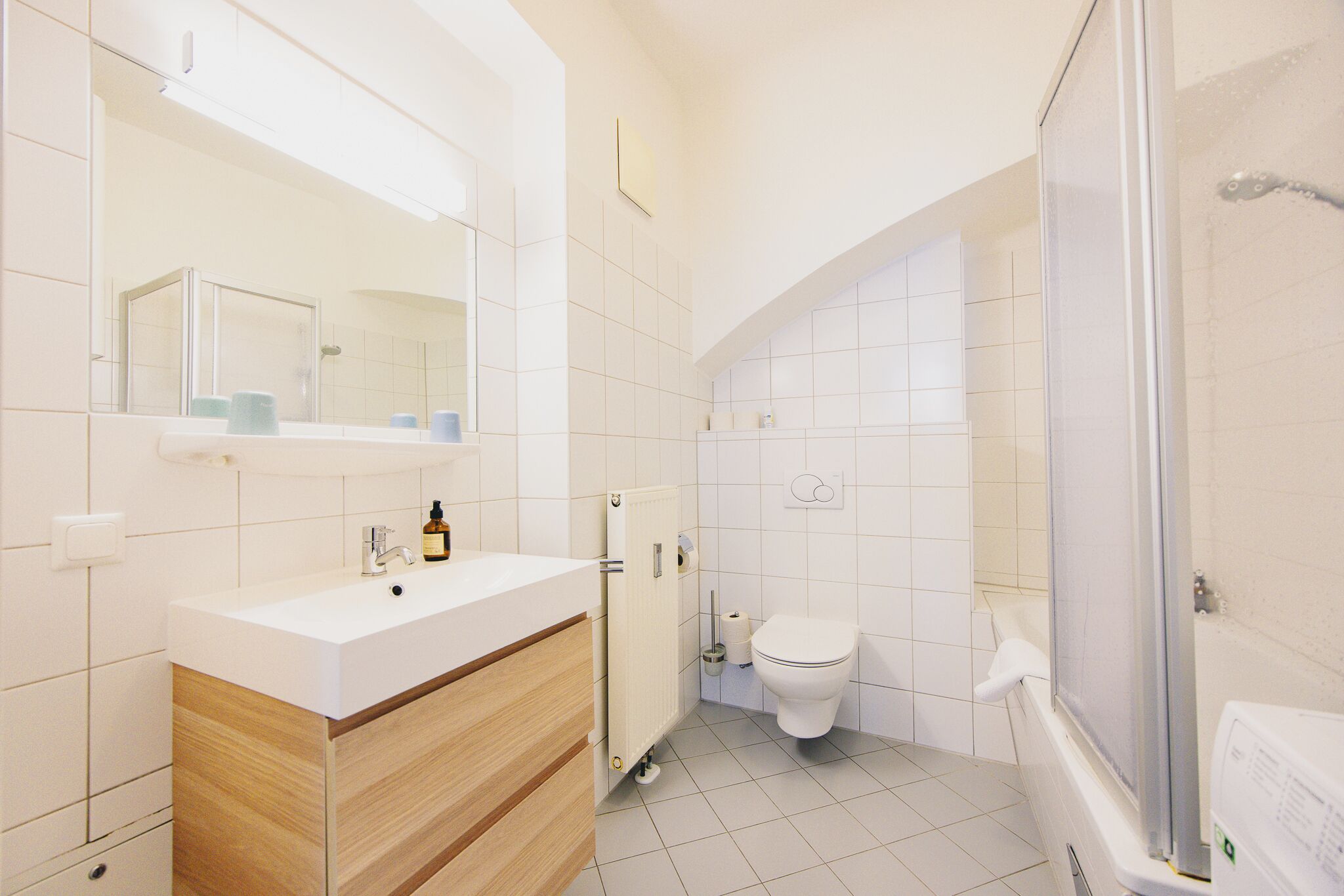 A modern bathroom with a white sink, mirror, toilet, and shower.
