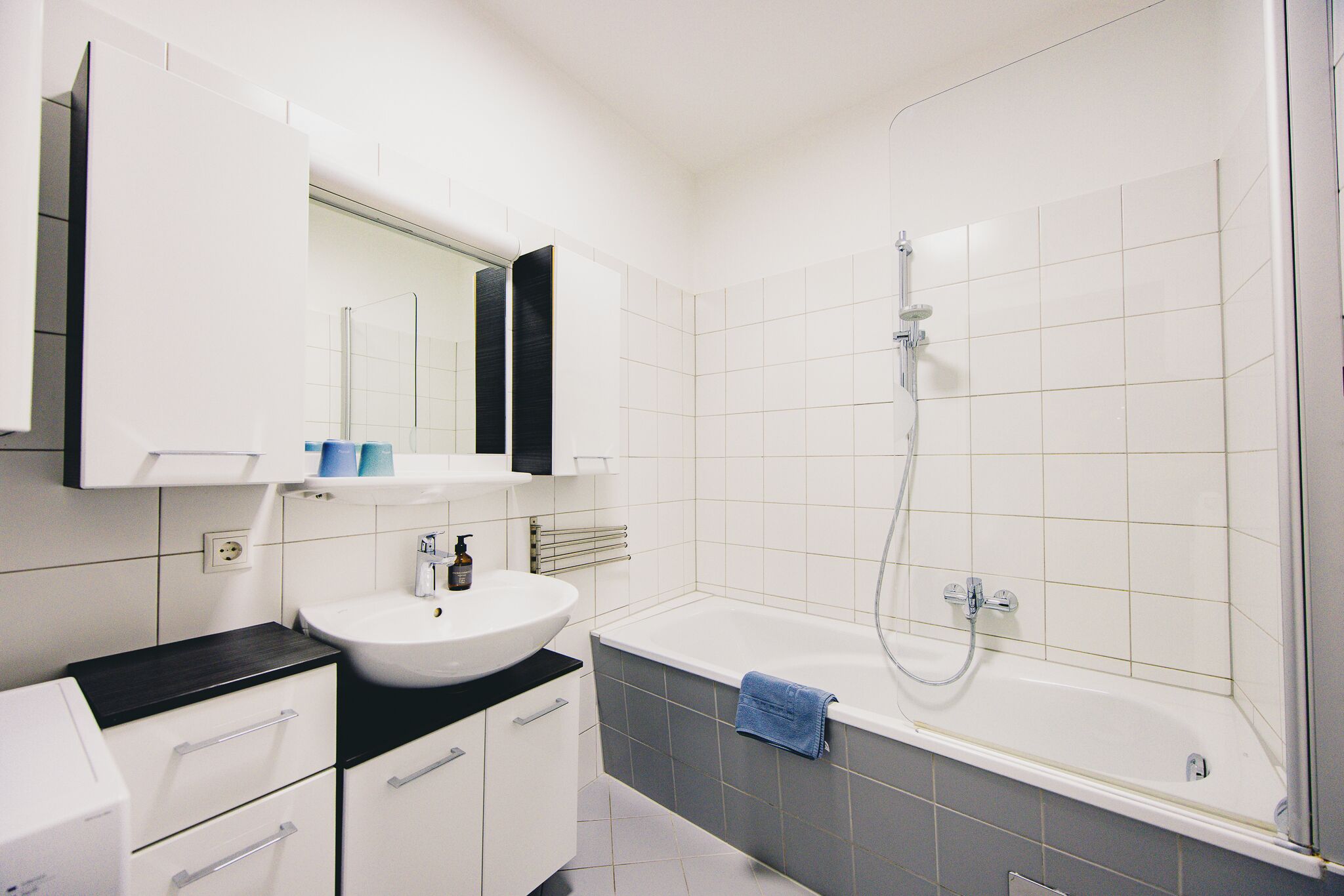 Une salle de bain moderne avec un lavabo blanc, un plan de toilette noir et une grande baignoire.