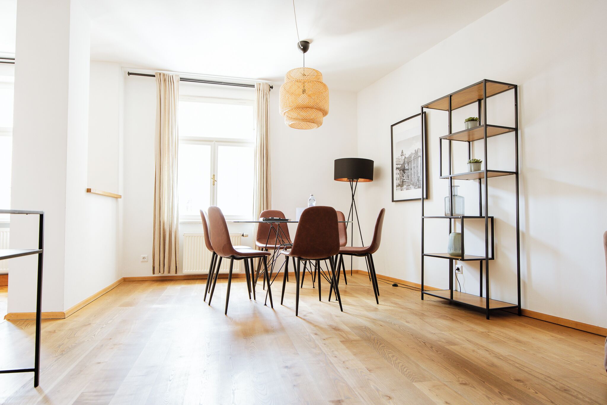 Et spiseområde med et bord, stole, en hængende lampe og en reol.