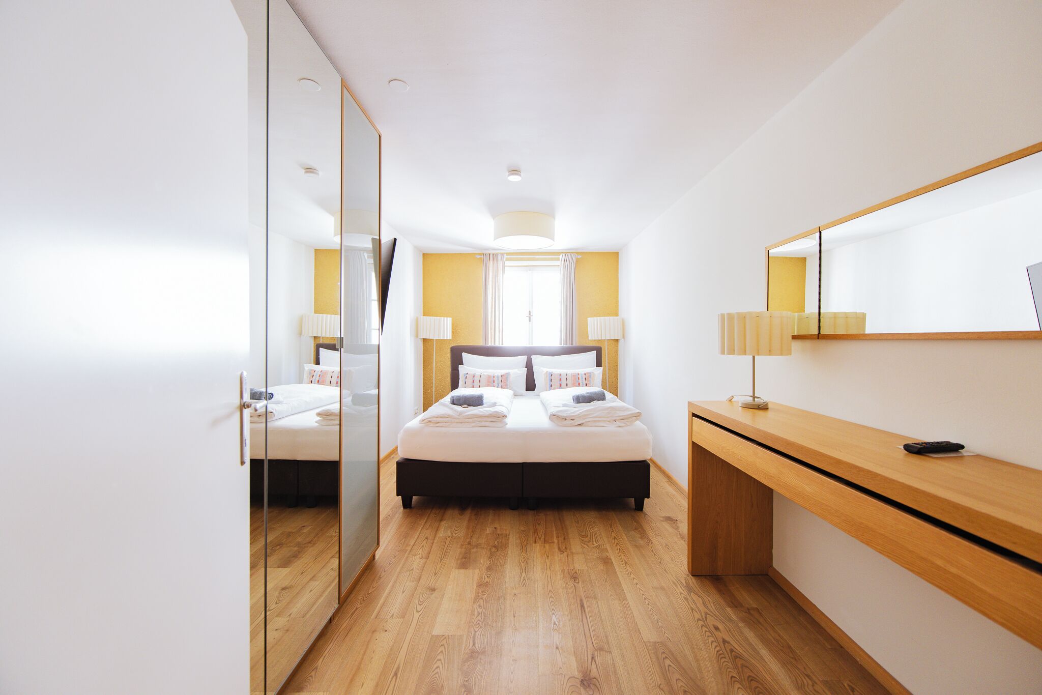 Een moderne slaapkamer met een bed, nachtkastjes, een spiegel en een houten bureau.