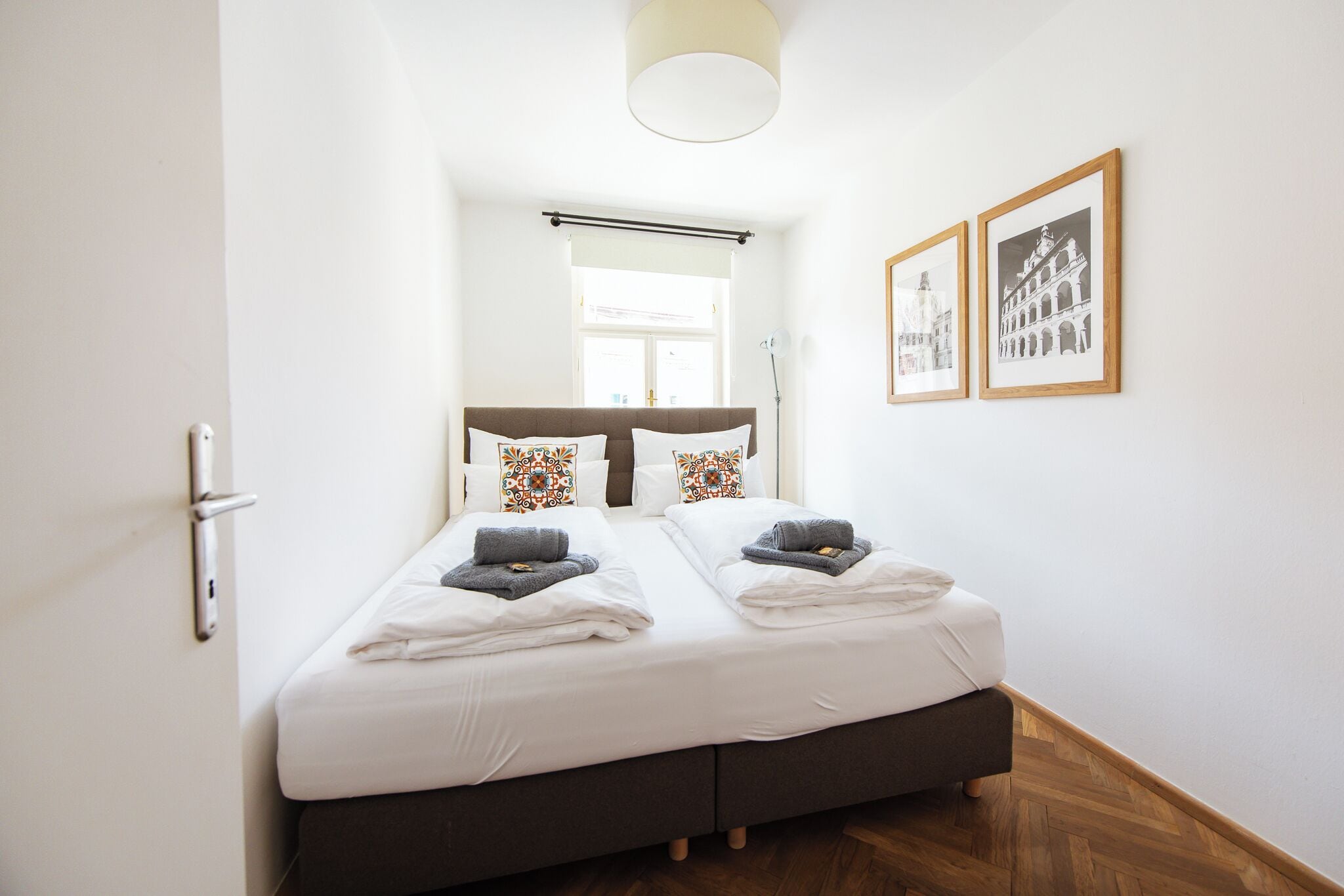 A hotel room with a bed, a window, and two framed pictures on the wall.