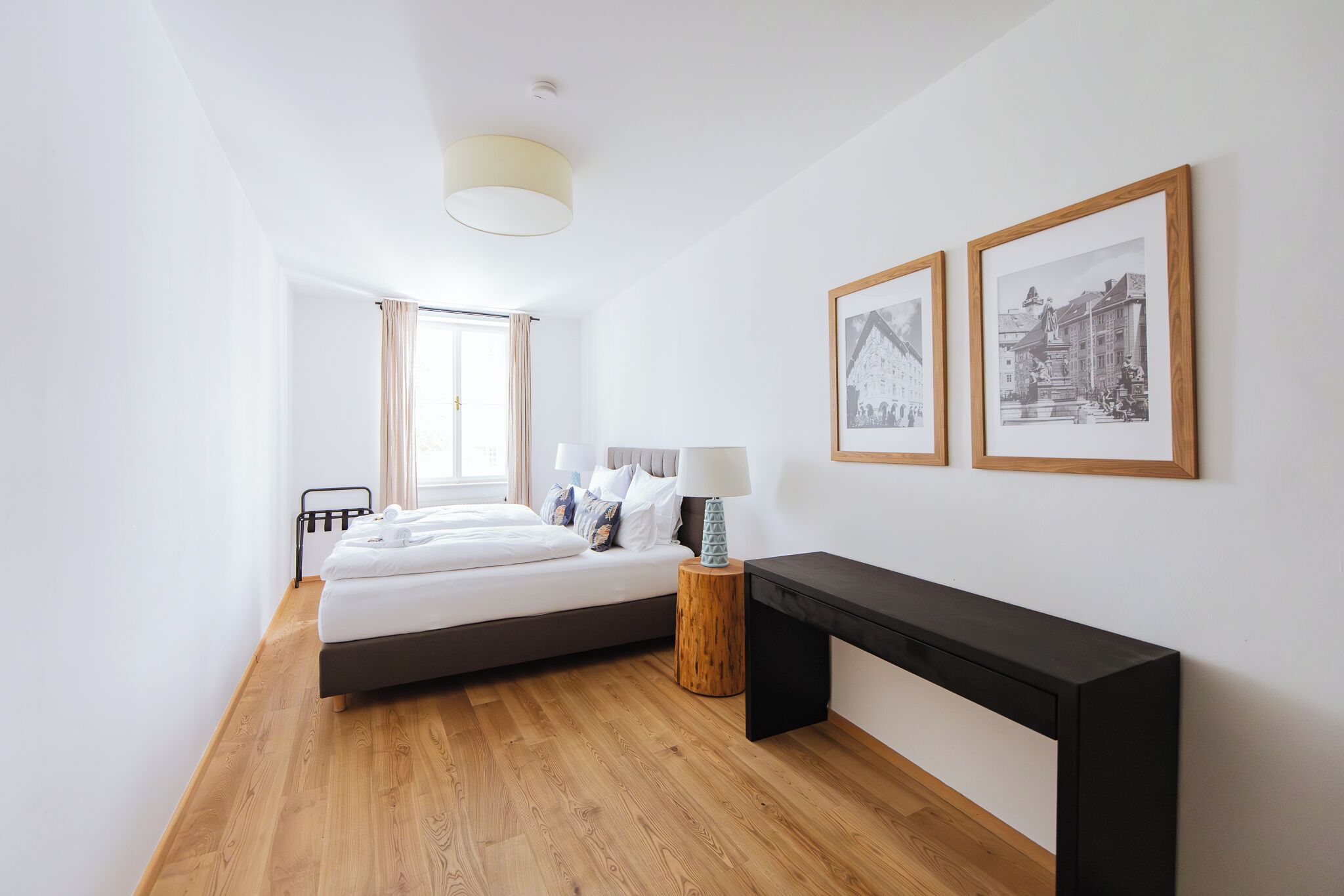 A modern bedroom with a bed, bedside table, lamp, and two framed pictures on the wall.