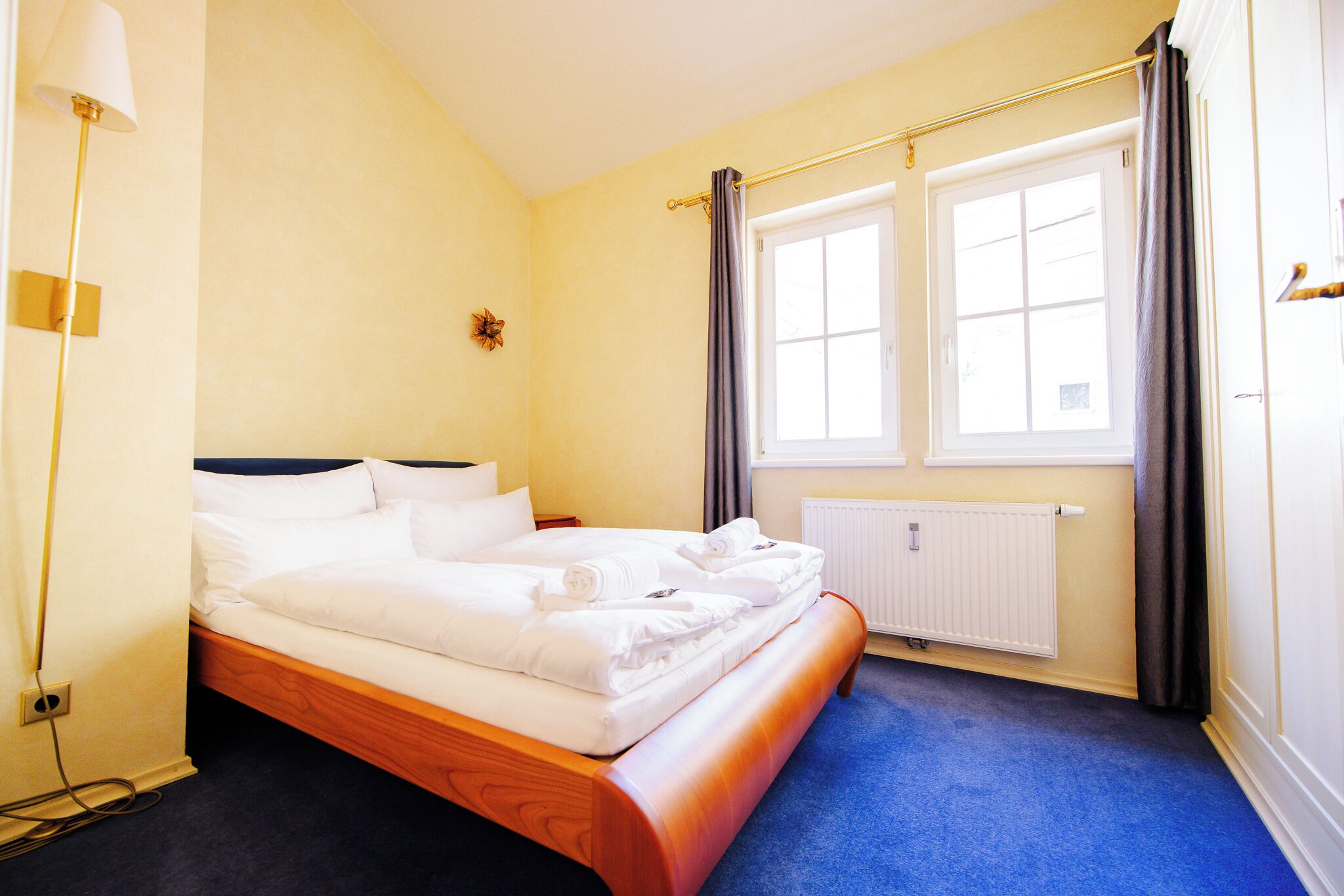 Hotellihuone, jossa on sänky, ikkuna, patteri ja lamppu.