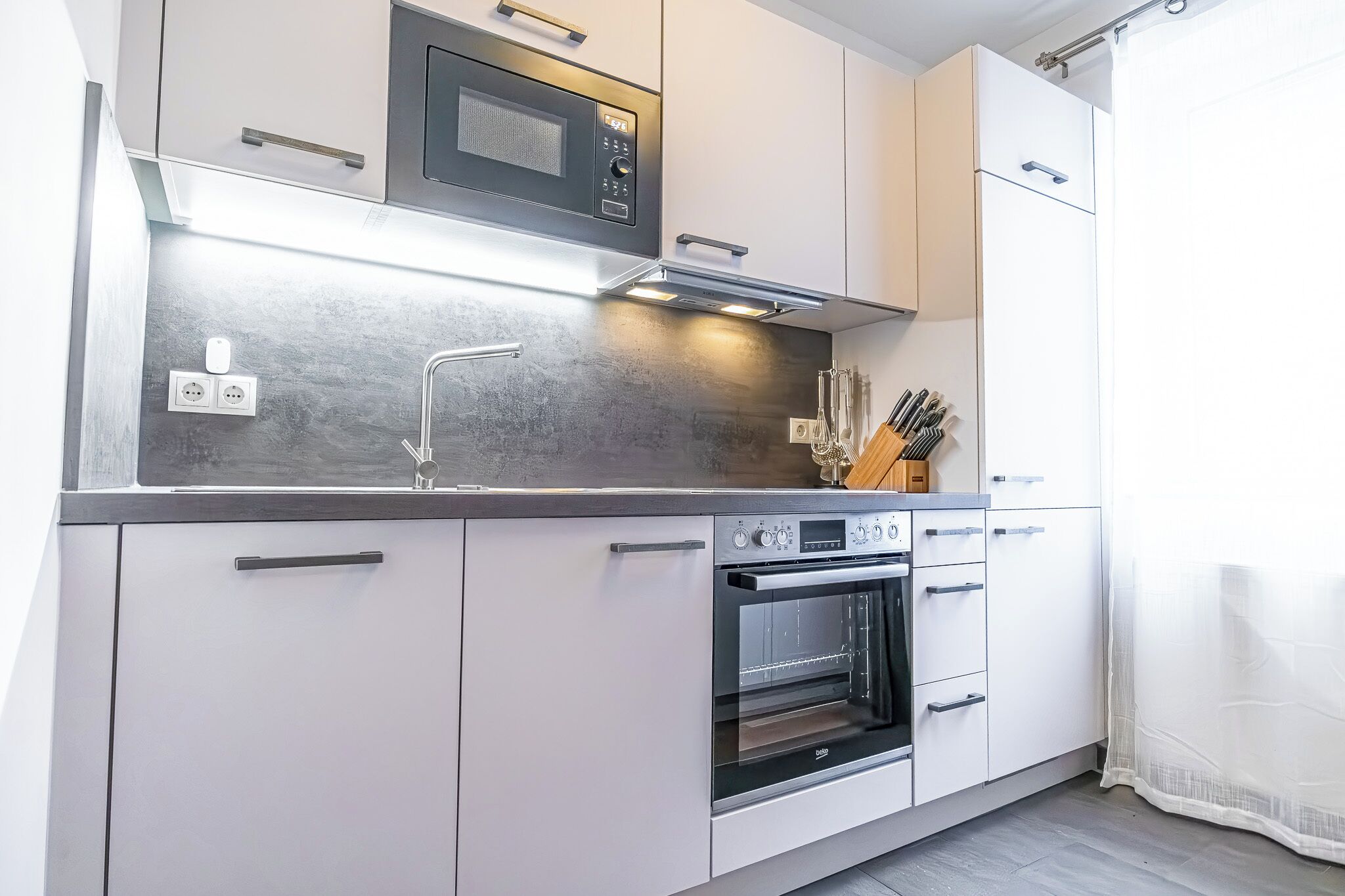 Una cocina moderna con horno integrado, microondas y encimera de acero inoxidable.