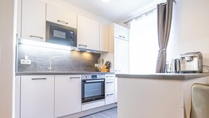 Una cocina moderna con armarios blancos, horno empotrado, microondas y cafetera.