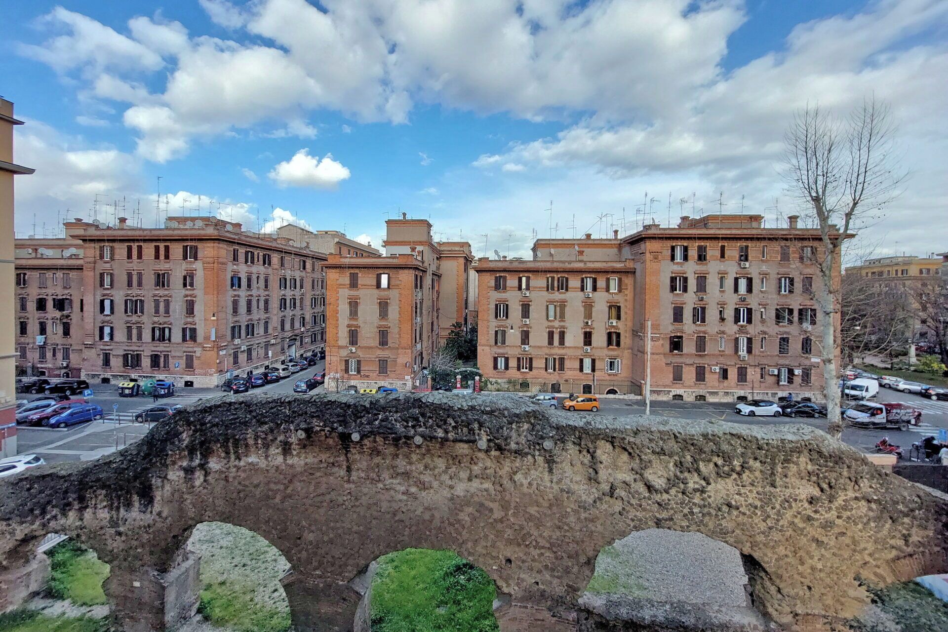 A multi-story building with a classical architectural style, featuring a central courtyard and a stone bridge in the foreground.