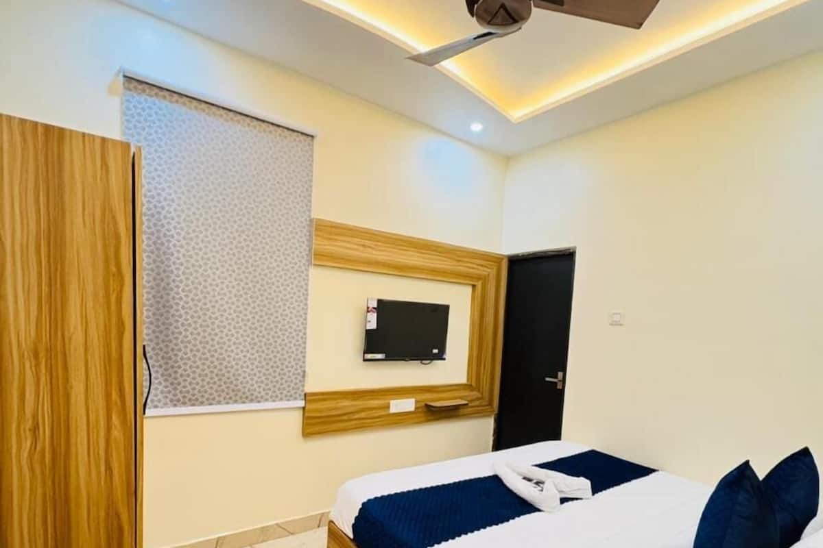 A modern hotel room with a bed, a ceiling fan, a mounted TV, and a wooden wardrobe.