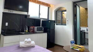 A modern kitchen with a flat-screen TV, a microwave, and a refrigerator. There is a window with blinds, a sink, and a towel on the counter. - Lunaria Maison - Central Park (Ho Chi Minh City)