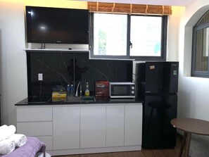 A compact kitchen with a flat-screen TV, a microwave, and a refrigerator. - Lunaria Maison - Saigon Central Park, District 3 (Ho Chi Minh City)