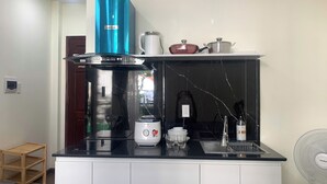 A kitchen with a black countertop, a stainless steel range hood, a coffee maker, a sink, and a fan. - Lunaria Maison - Central Park (Ho Chi Minh City)
