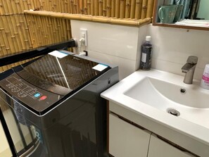 A bathroom with a black washing machine, a white sink, and a bamboo shelf. - Lunaria Maison - Saigon Central Park, District 3 (Ho Chi Minh City)