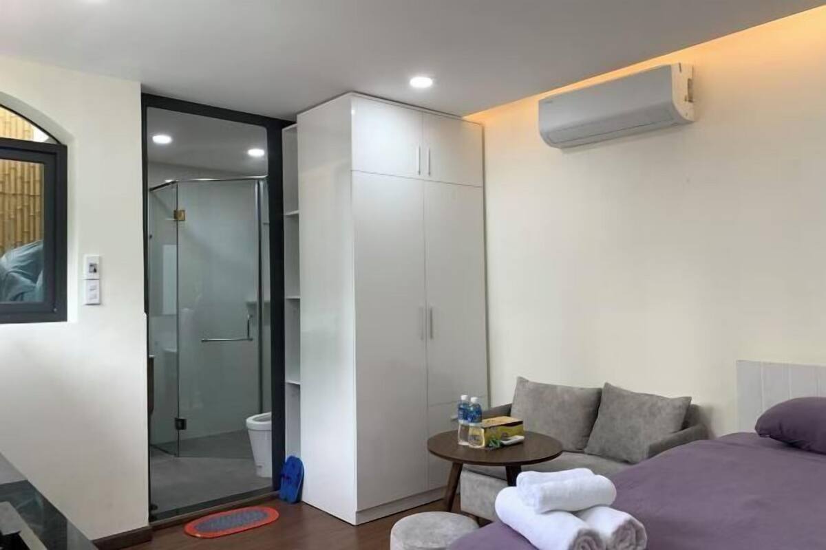 A hotel room with a bed, a small table with toiletries, a wardrobe, and a glass shower enclosure.