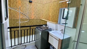 A modern bathroom with a bamboo wall, a glass shower enclosure, and a compact sink area. - Lunaria Maison - Central Park (Ho Chi Minh City)