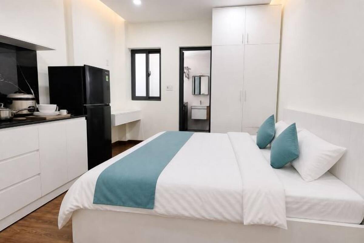 A bedroom with a bed, a nightstand, a window, and a door leading to a bathroom.