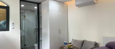 A hotel room with a bed, a small table with toiletries, a wardrobe, and a shower area.