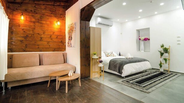 A modern bedroom with a wooden ceiling, a bed with a gray and white duvet, a small bedside table, and a floor-to-ceiling mirror. - Luxury Suite in Tiberias (Tiberias)