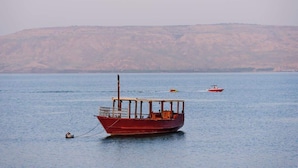 A red boat anchored in calm waters with a hilly landscape in the background. - Luxury Suite in Tiberias (Tiberias)