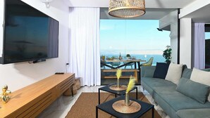 A modern living room with a large TV, a wooden bench, a sofa, and a dining area with a view of the sea. - Villa Selavi  Private Infinity Pool (Tiberias)