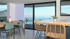 A modern dining area with a view of the ocean, featuring a wooden table, wicker chairs, and a potted plant. - Villa Selavi  Private Infinity Pool (Tiberias)