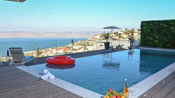 A pool with a view of the sea, a red inflatable ring, a bottle of champagne, and a fruit bowl. - Villa Selavi  Private Infinity Pool (Tiberias)