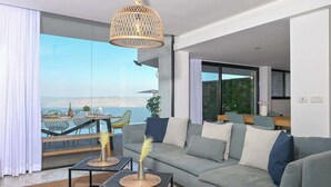 A modern living room with a large sofa, two coffee tables, and a dining area with a table and chairs. - Villa Selavi  Private Infinity Pool (Tiberias)