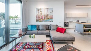 Ein modernes Wohnzimmer mit einem grauen Ecksofa, einem farbenfrohen Teppich und einem großen Fenster.