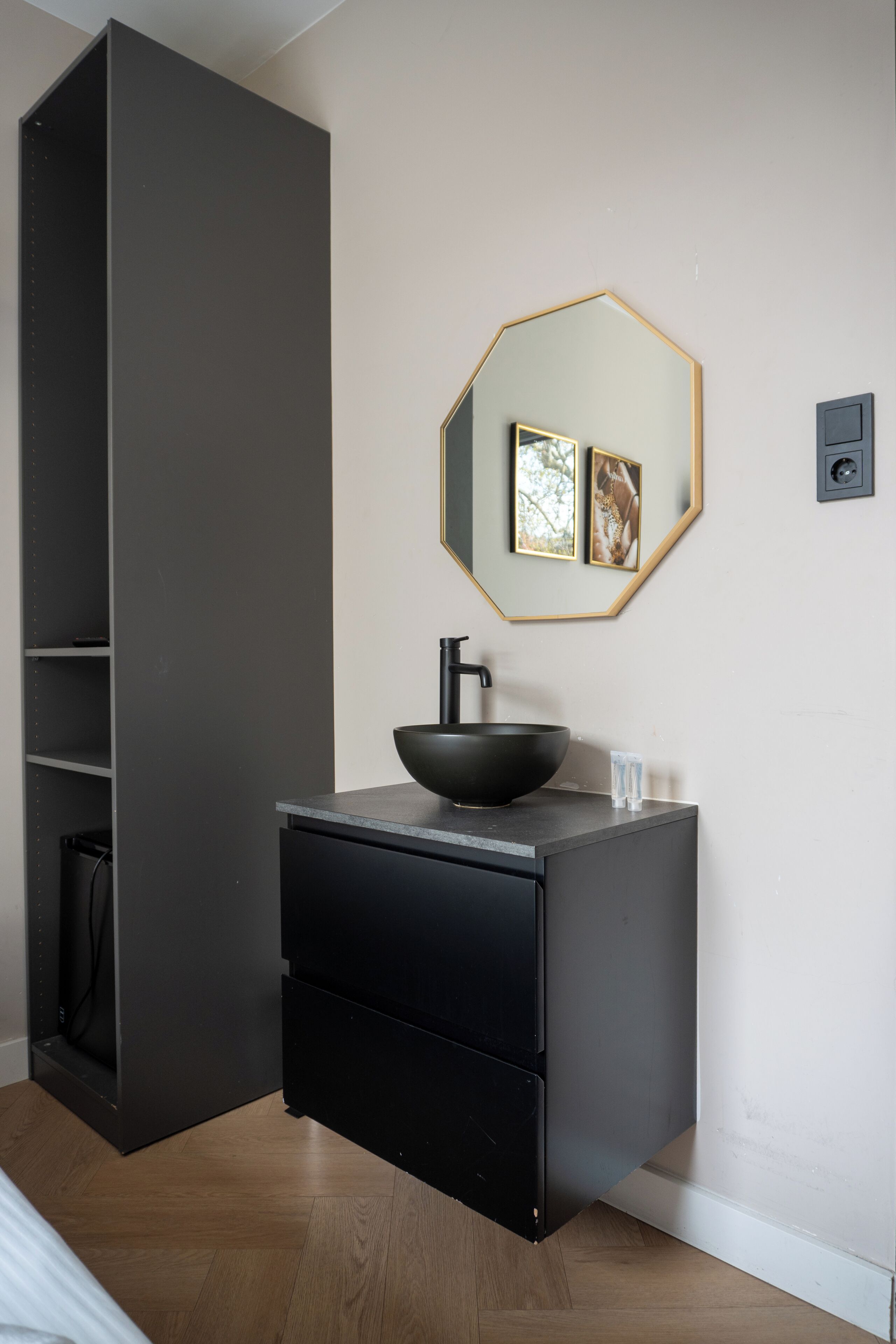 A modern bathroom with a black sink, a mirror with a gold frame, and a wooden floor.