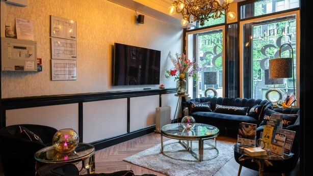 A modern lounge area with a black sofa, a glass coffee table, and a chandelier. - Hotel 83 (Amsterdam)