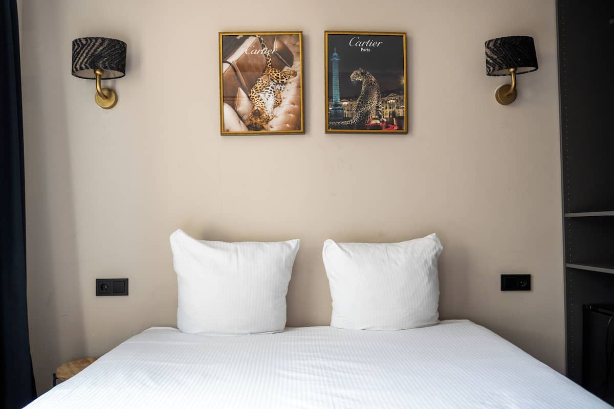A hotel room with a bed, two wall-mounted lamps, and two framed posters.