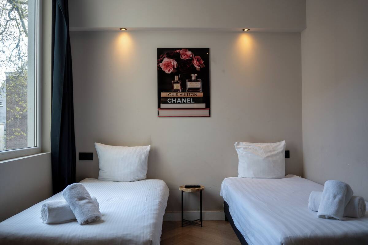 A hotel room with two beds, a small table, and a poster on the wall.