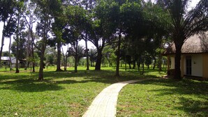 A pathway leading through a park with trees and a building with a thatched roof. - Gray Hideaway Resort (Kayunga)