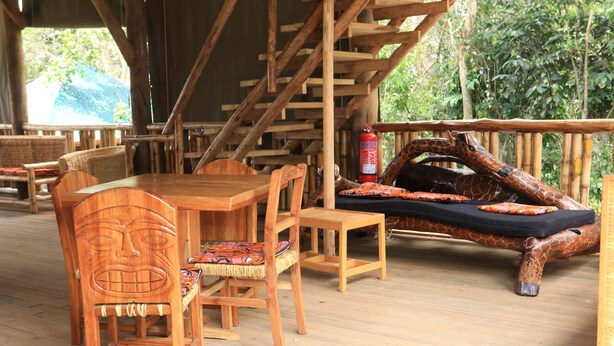 A wooden deck with a dining table and chairs, a sofa with a giraffe design, and a fire extinguisher. - Gray Hideaway Resort (Kayunga)