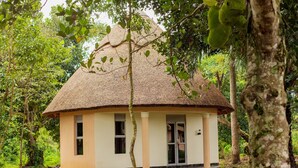 A thatched-roof hut with a single door and windows, surrounded by lush greenery. - Gray Hideaway Resort (Kayunga)