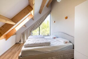 Un dormitorio con techo inclinado, una cama, un ventanal y estructura de vigas de madera.
