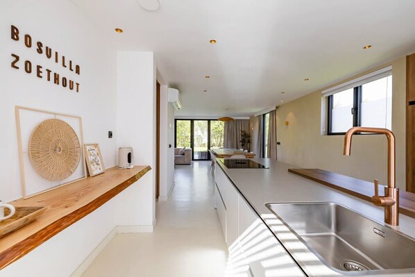 Una cocina moderna con una isla central, lavamanos de acero inoxidable y vistas a un comedor.