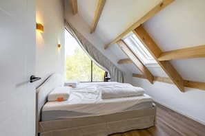 Ein Schlafzimmer mit schrägem Dach, einem Bett, einem Fenster und einer Tür.