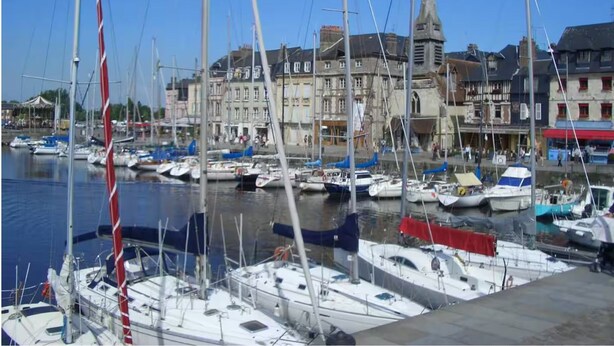 A marina with multiple sailboats docked, a prominent church with a tall spire, and buildings with traditional architecture. - Modern studio with terrace 5 min from Honfleur parking and swimming pool (Équemauville)