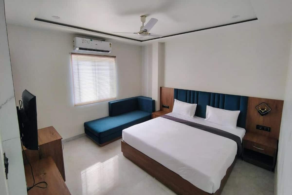 Ein Hotelzimmer mit einem Bett, einem blauen Sofa, einem Fernseher, einer Klimaanlage und einem Deckenventilator.