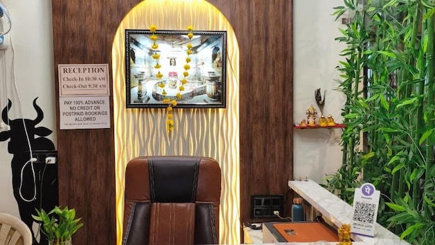 A reception desk with a modern design, a framed picture above it, and a check-in/out schedule on the wall. - Hotel Gurukripa (Ujjain)