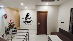 A modern interior with a wooden door, a staircase with metal railings, and a wall-mounted fire extinguisher. - Hotel Gurukripa (Ujjain)