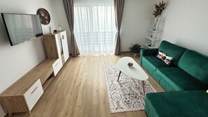 Ett modernt vardagsrum med en grön soffa, en platt-TV, trämöbler och ett stort fönster med gardiner.