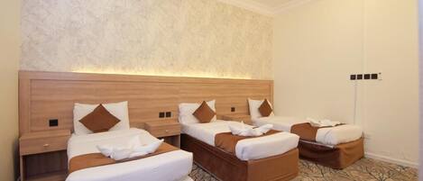 A hotel room with three beds, a wooden headboard, a patterned carpet, and a light fixture on the ceiling.