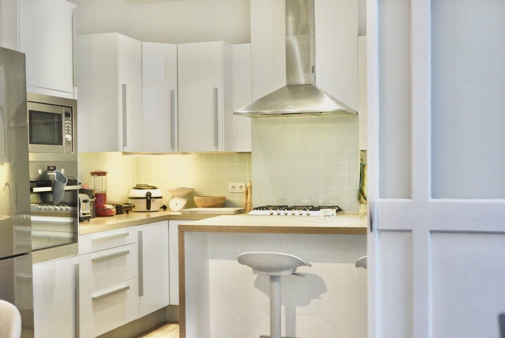 Une cuisine moderne avec des meubles blancs, une hotte en acier inoxydable et un four encastré.