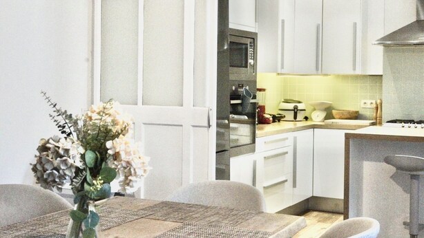 A modern kitchen with white cabinets, a microwave, and a stove. There is a dining area with a table and chairs. - Spacious 3-bedroom apartment in the heart of Brussels for 8 people (Bruxelles)